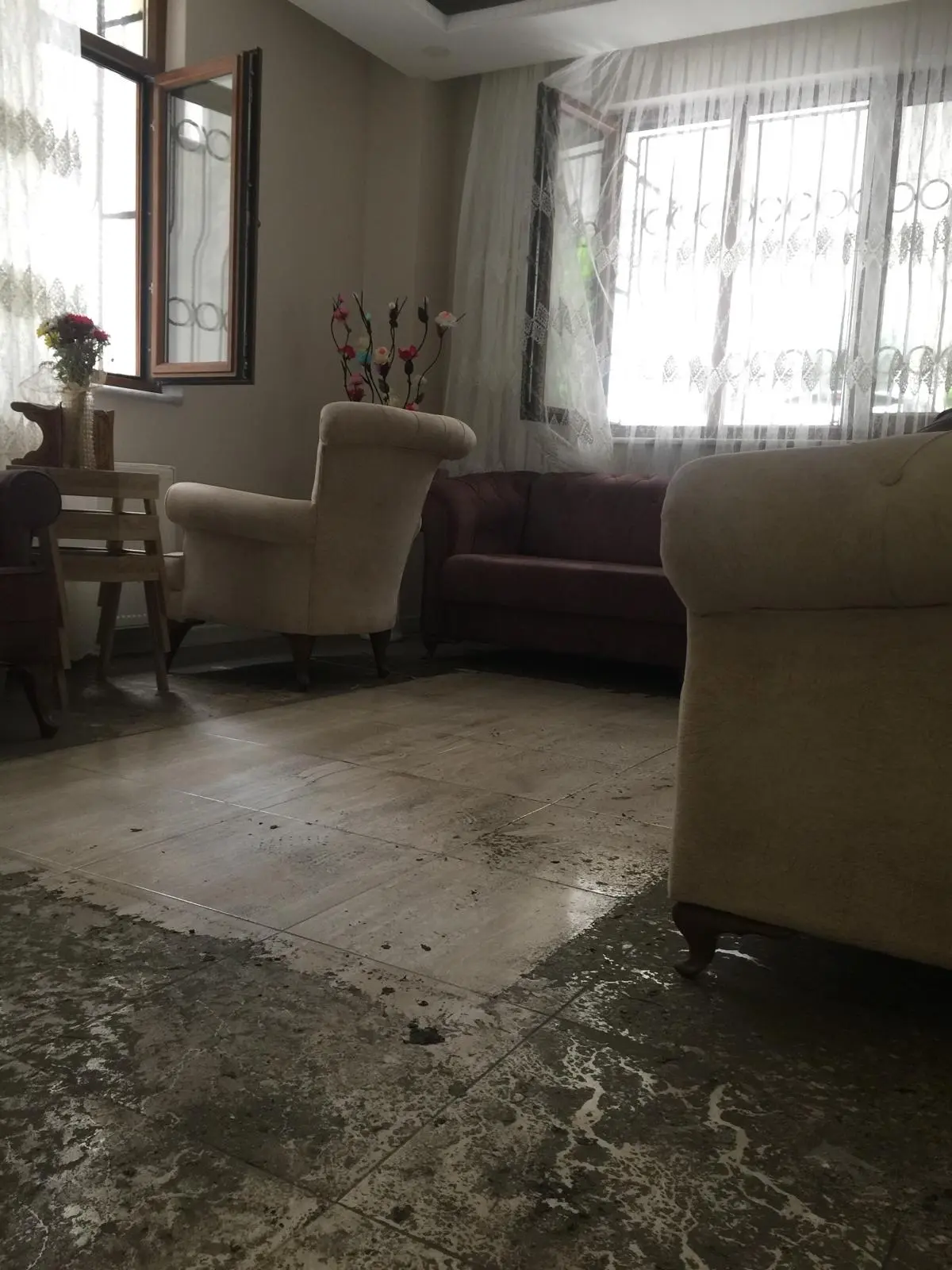 Ev temizliği öncesinde zeminde yoğun kir, çamur ve temizlik kalıntıları bulunan salon alanı