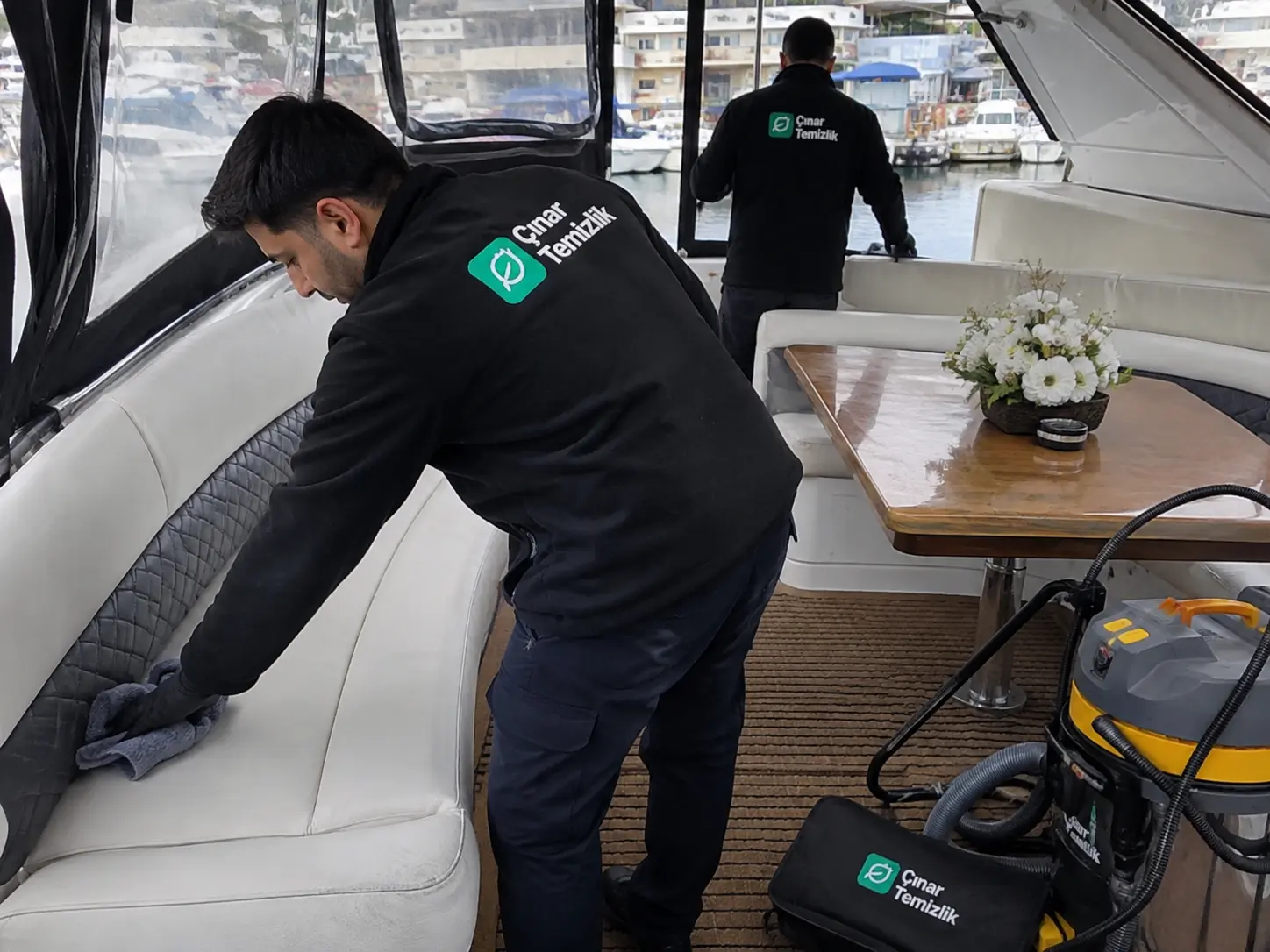 Marinada bağlı gerçek bir yat veya orta-büyük teknede Çınar Temizlik personeli iç salon veya açık oturma alanında aktif temizlik yapıyor.