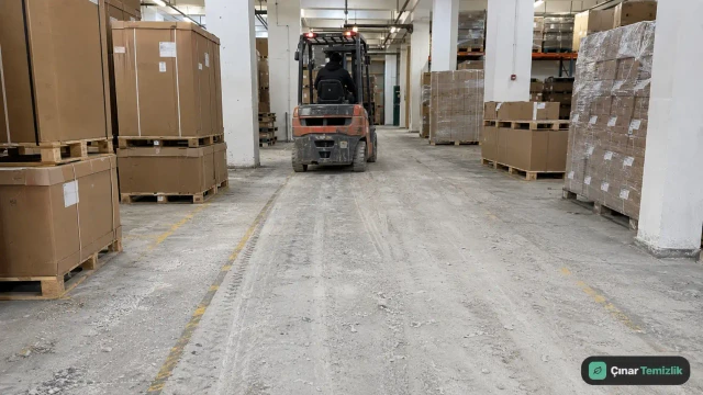 Forklift trafiğiyle koridora yayılan gri beton tozu bulunan depo zemini